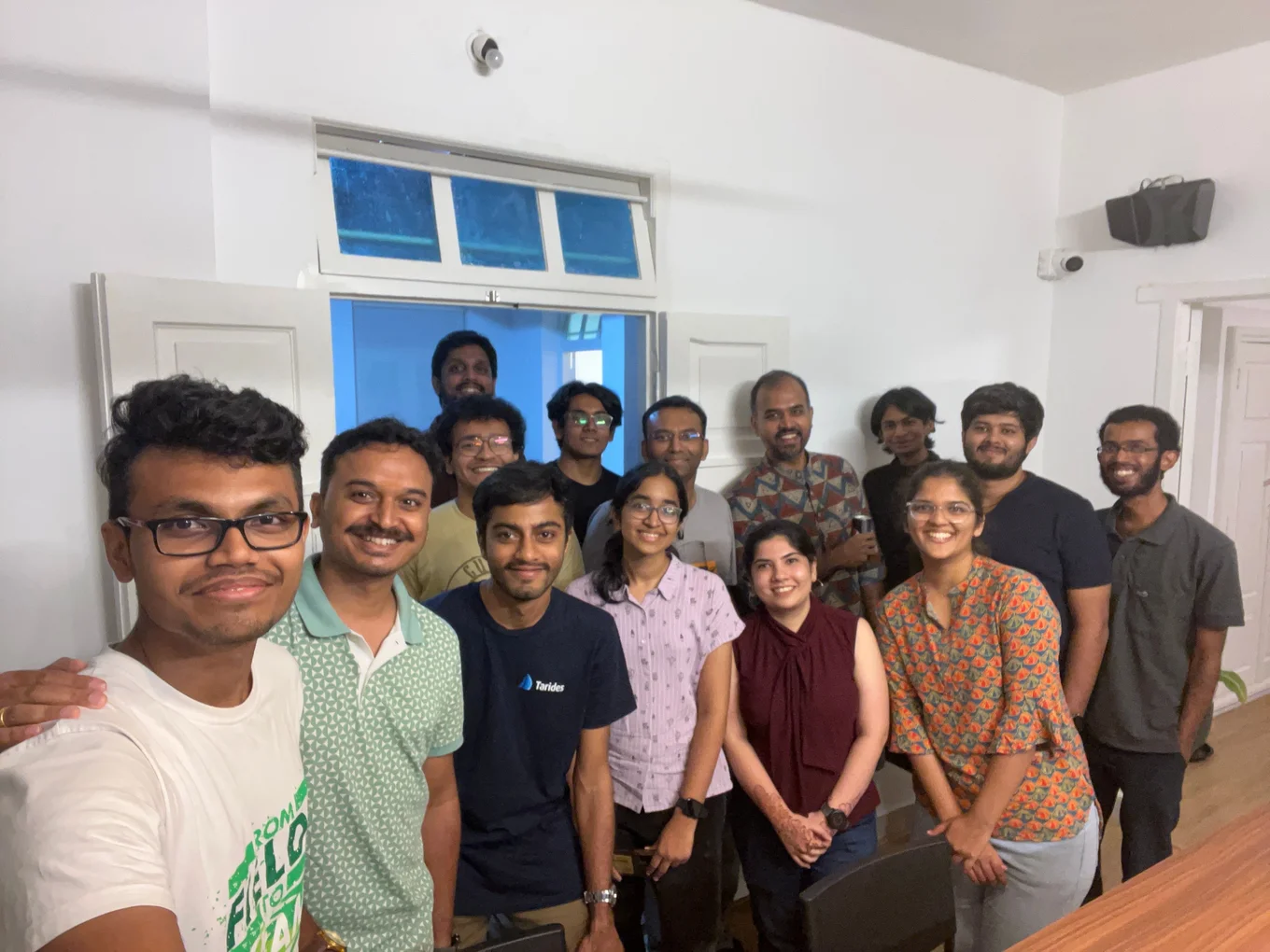 A group of 13 people smiling indoors.
