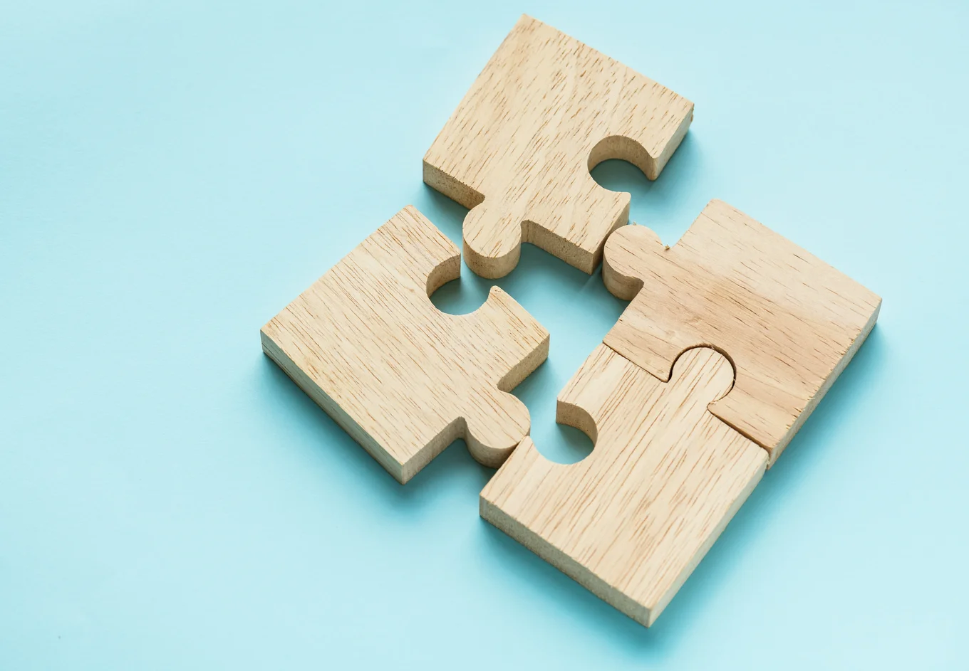 Four pieces of a half-solved wooden jigsaw puzzle against a blue background